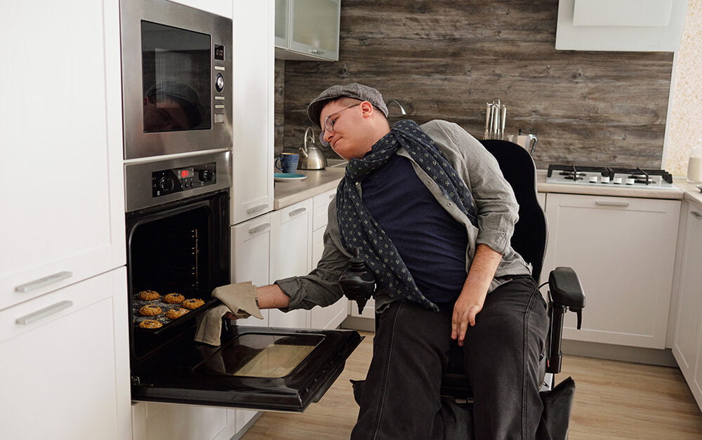 Image of man in wheelchair at home in kitchen with NDIS home modifications, taking homemade biscuits out of the oven