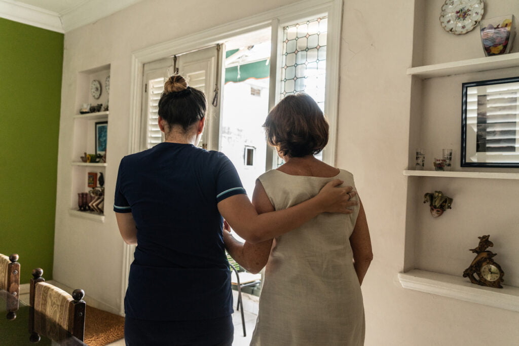 Home caregiver helping woman to walk at home