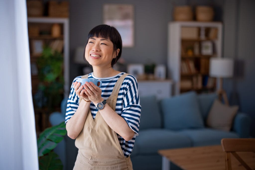 Happy woman standing in living room holding coffee cup
