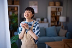 Happy woman standing in living room holding coffee cup