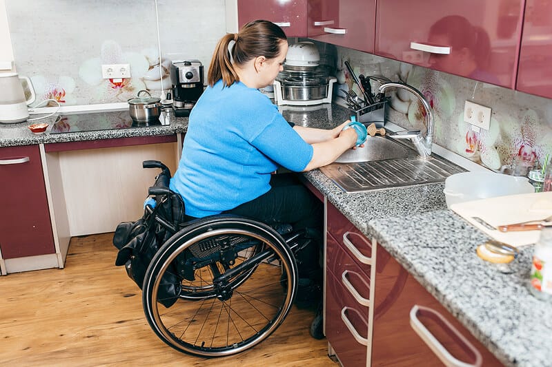 A woman in a wheelchair washing dishes at an accessible kitchen sink
